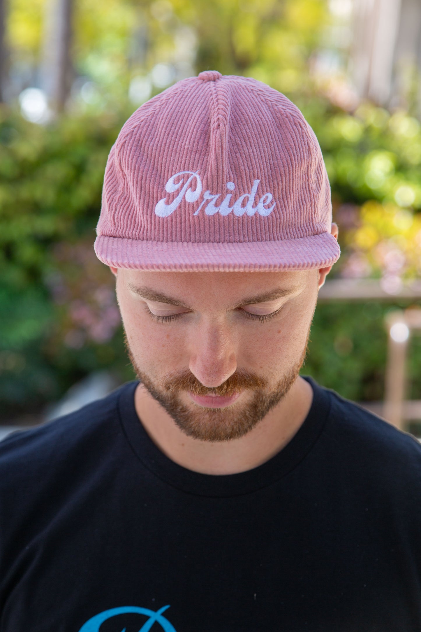 Person wearing the pink <Insert Material Type> hat with the text "Pride" on the front outside.